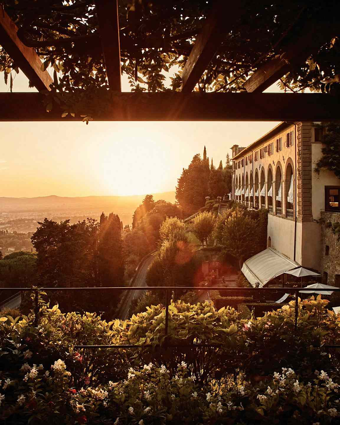 En terrass omgiven av grönska med utsikt över en stad i solnedgången. (AI-genererad text)