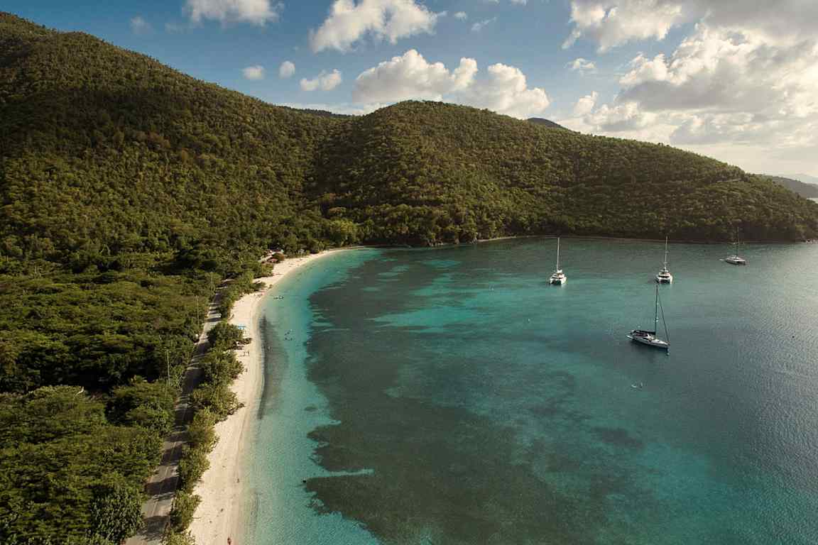 Vy över en strand med turkost vatten och båtar samt gröna kullar i bakgrunden. (AI-genererad text)