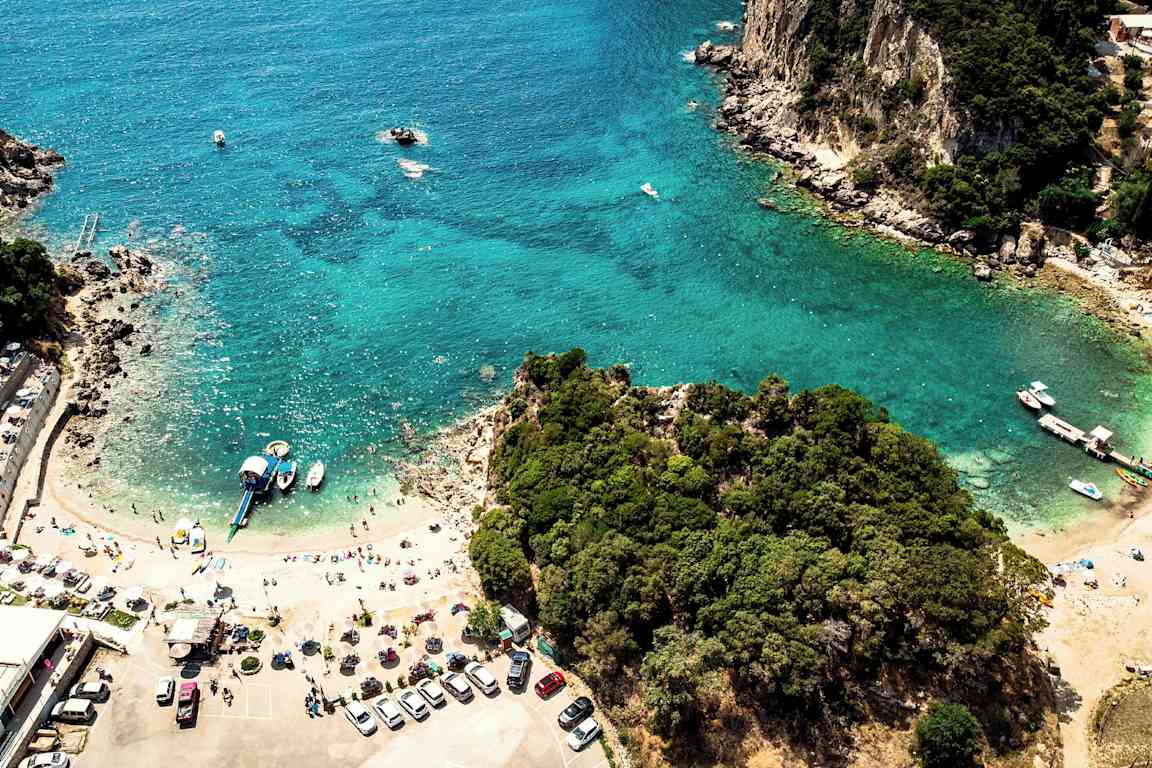 Flygbild av en strand med klarblått vatten, omgiven av grönska och några båtar vid strandlinjen. (AI-genererad text)
