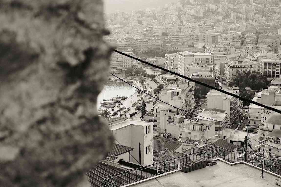 Bild på en stad med många byggnader, en hamn och båtar, sedd från en högre position, med en suddig förgrund. (AI-genererad text)