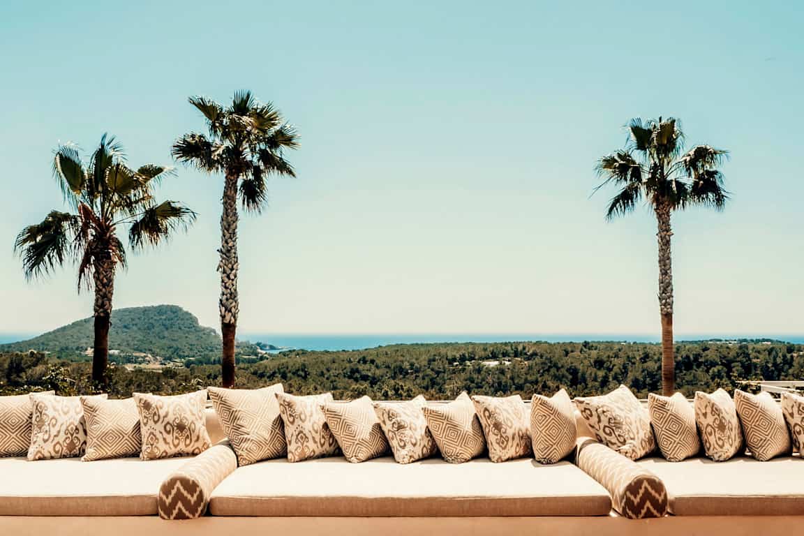 Palmträd och soffan med kuddar mot utsikt över landskapet. (AI-genererad text)