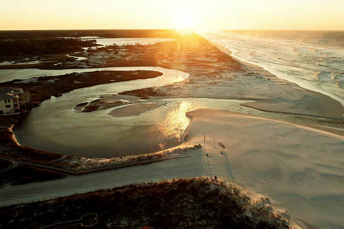 Solnedgång över ett landskap med flod, sanddyner och hav. (AI-genererad text)