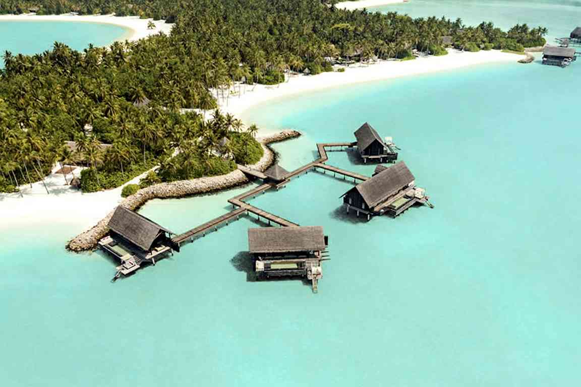 Flygvy över tropisk ö med vattenbungalower vid stranden och omgivande palmträd. (AI-genererad text)