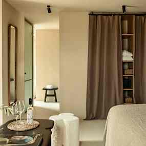 Ett sovrum med neutral inredning, inklusive en säng, gardiner och dekorativa detaljer. (AI-genererad text)