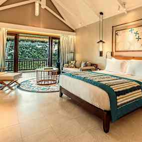 Hotellrum med dubbelsäng, sittgrupp och utsikt över grönskande natur. (AI-genererad text)