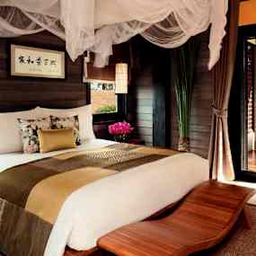 Ett sovrum med en stor bekväm säng, dekorerad med sängöverkast och kuddar, samt nät ovanför sängen. (AI-genererad text)