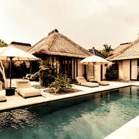 Bild av en pool framför en tropisk villa med solstolar och parasoller. (AI-genererad text)