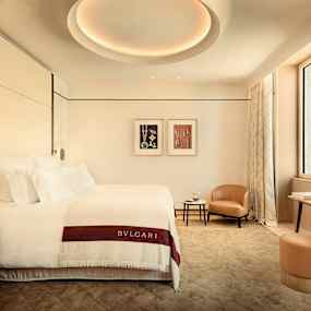 Ett elegant hotellrum med en bäddad säng, sidobord, fåtölj och ett arbetsbord. (AI-genererad text)