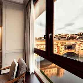 Ett rum med moderna möbler och stora fönster som vetter mot en vacker stadsutsikt, inklusive en historisk bro över en flod. (AI-genererad text)