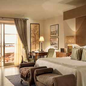 Ett hotellrum med en bekväm dubbelsäng, sittmöbler och skrivbord. Ett stort fönster med gardiner leder ut till en möblerad balkong. (AI-genererad text)