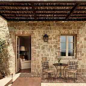 En uteplats med stenvägg, ett litet bord med två stolar och en soffa med kuddar. (AI-genererad text)