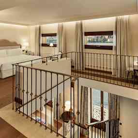 Bild på ett hotellrum med en dubbelsäng, fönster med utsikt mot vattnet och en inomhustrappa. (AI-genererad text)