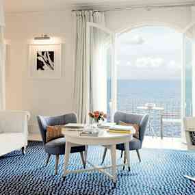 Interiör av ett ljust rum med blå matta, vita möbler och havsutsikt. (AI-genererad text)