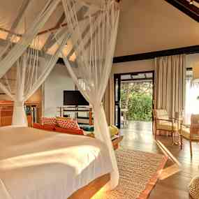 Ett sovrum med en himmelsäng och sittgrupp, med utsikt mot en grönskande trädgård. (AI-genererad text)