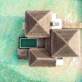 Flygfoto av en bungalow med halmtak, omgiven av turkost vatten. (AI-genererad text)