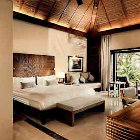 Välutrustat hotellrum med dubbelsäng, sittgrupp, skrivbord och balkong mot grönskande trädgård. (AI-genererad text)