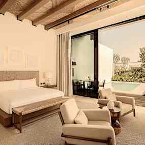 Hotellrum med dubbelsäng, sittmöbler och utsikt mot en privat pool. (AI-genererad text)