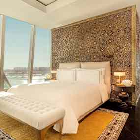 Lyxigt sovrum med utsikt över havet, stor säng med vita lakan, dekorativ huvudgavel och elegant inredning. (AI-genererad text)