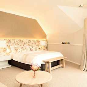 Ett ljust sovrum med blommigt huvudgavel, stor säng och fönster med gardiner. (AI-genererad text)