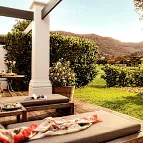 En terrass med vilstolar, bord och en grön trädgård med utsikt mot berg. (AI-genererad text)