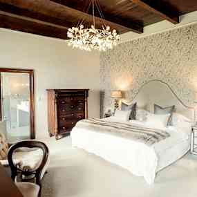 Ett elegant sovrum med en dubbel säng, dekorativa lampor och en detaljerad tapet på väggen. (AI-genererad text)