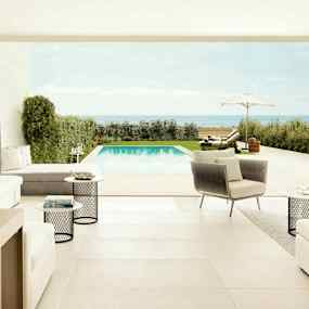 Utsikt från en modern, ljus inomhusmiljö med soffor och bord, mot en terrass med pool och utsikt över havet. (AI-genererad text)