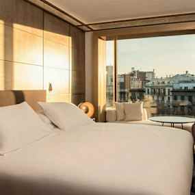 Hotellrum med en stor säng, fåtölj och utsikt över en stad. (AI-genererad text)