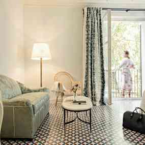 Elegant hotellrum med en soffa, fåtölj, golvlampa och bord på mönstrad golvyta. (AI-genererad text)