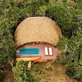 Luftbild av en bungalow med halmtak, omgiven av skog, med en träterrass och en liten pool. (AI-genererad text)