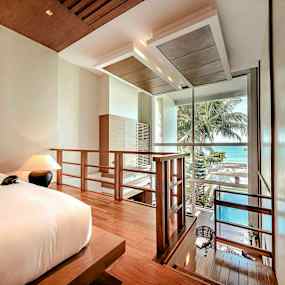 Ett hotellrum med en säng, lampor och en trappa som leder ner mot en balkong med utsikt över havet. (AI-genererad text)