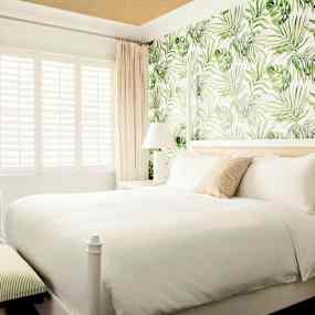 Sovrum med en dubbelsäng, väggar med grönt lövmotiv och möbler i ljusa färger. (AI-genererad text)
