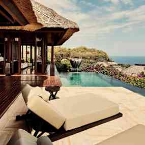 Utsikt över en utomhusterrass med solstolar och pool, omgiven av växtlighet och hav i bakgrunden. (AI-genererad text)