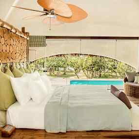 Ett välutrustat sovrum med en träinramad säng, stora fönster och utsikt över en pool. (AI-genererad text)