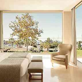 Hotellrum med en stor säng och sittmöbler samt utsikt över en grönskande trädgård och småbåtshamn. (AI-genererad text)