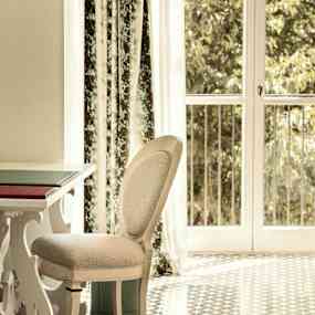 Ett rum med en stol och bord nära ett fönster med gardiner och utsikt över träd. (AI-genererad text)