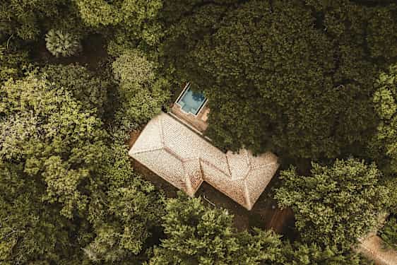 Luftperspektiv av en byggnad med tegeltak omgiven av tät grönska, en liten blå pool syns nära byggnaden. (AI-genererad text)