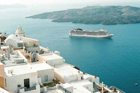 En kryssningsfartyg seglar förbi vita byggnader vid kusten. (AI-genererad text)