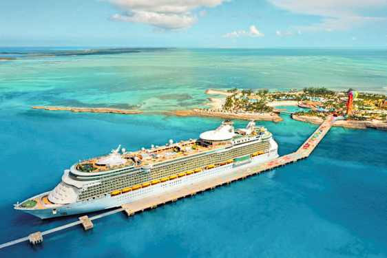 Ett kryssningsfartyg ligger vid en kaj i en tropisk miljö med turkost vatten och öar i bakgrunden. (AI-genererad text)