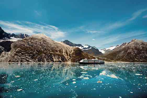 Ett kryssningsfartyg på en stilla sjö omgivet av berg och isflak. (AI-genererad text)