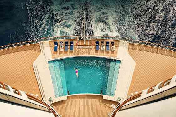 Vy uppifrån av ett fartygsdäck med pool och solstolar, vatten bakom. (AI-genererad text)