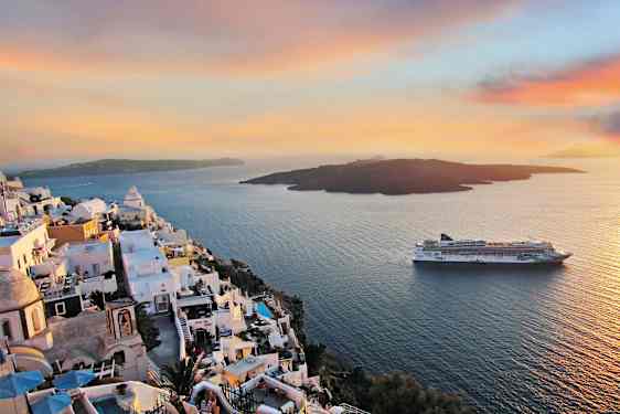 Vitkalkade byggnader på en klippa ovanför havet med en kryssningsfartyg i bakgrunden under en färgrik solnedgång. (AI-genererad text)