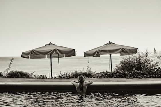Person i pool med parasoller och havet i bakgrunden. (AI-genererad text)