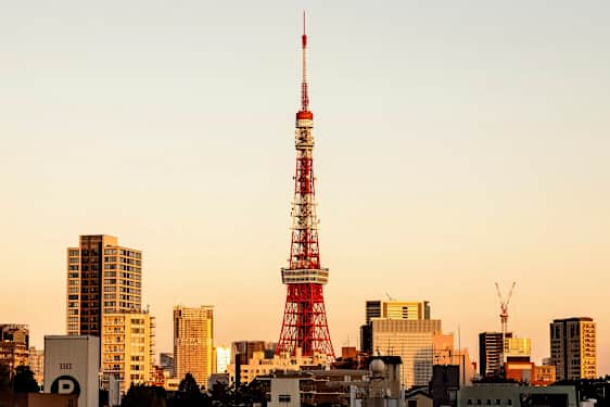 En vy över Tokyo Tower omgivet av byggnader vid solnedgången. (AI-genererad text)