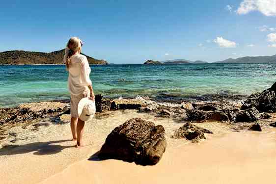 En kvinna står på en sandstrand och tittar ut över havet, omgiven av klippformationer. (AI-genererad text)
