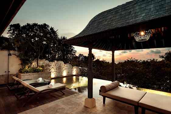 En lyxig uteplats vid poolen under tak med solstolar och en pittoresk solnedgång i bakgrunden. (AI-genererad text)