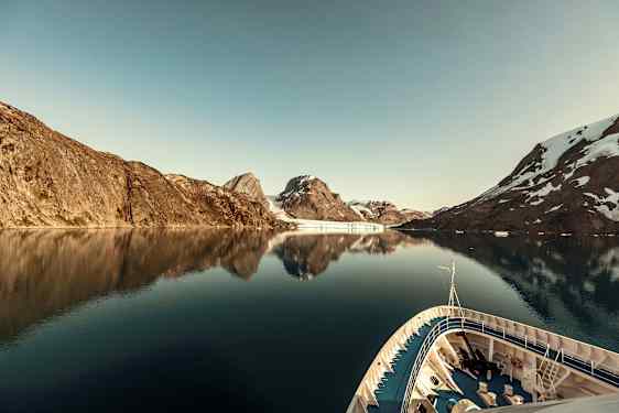 Ett fartyg i en lugn fjord omgiven av berg med snö. (AI-genererad text)