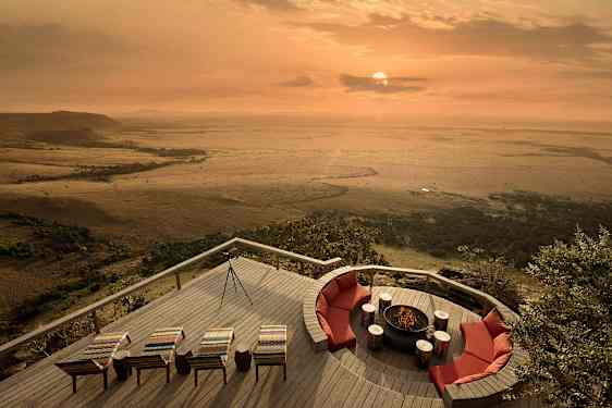 Utomhusterrass med sittplatser och eldplats, med utsikt över en savann vid solnedgång. (AI-genererad text)