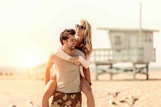 En person ger en annan person en ryggtur på en strand vid solnedgången. (AI-genererad text)