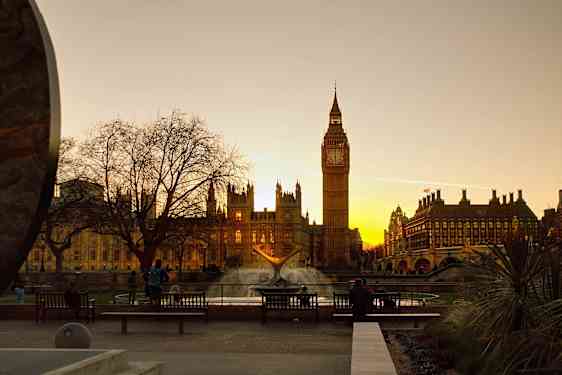 Vy över Big Ben och Westminster vid solnedgången, med en fontän i förgrunden. (AI-genererad text)
