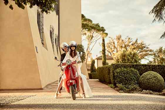 Två personer åker på en röd moped genom en elegant gård. (AI-genererad text)